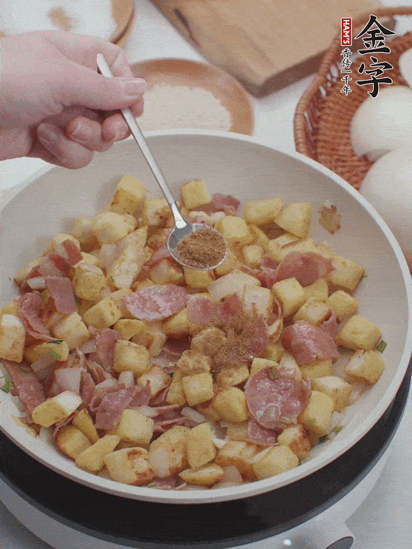 起鍋少油，煸香洋蔥丁、蔥白，加入金字培根火腿翻炒幾下，再加入饅頭丁、1小勺孜然粉、少許鹽翻炒均勻并鋪平。